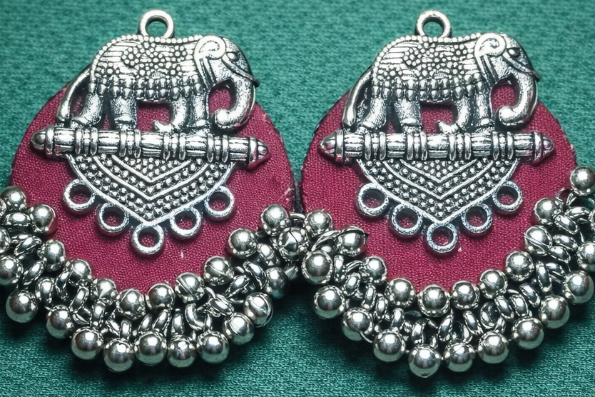 Pair of silver earrings with elephant design on a teal background